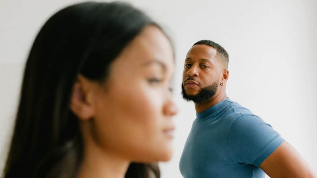 A man in a blue shirt looks toward a woman who is blurred in the foreground.