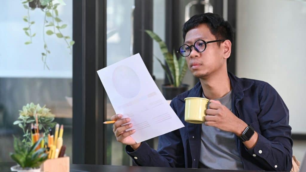 A man wearing glasses and a navy shirt holds a yellow mug and a document.