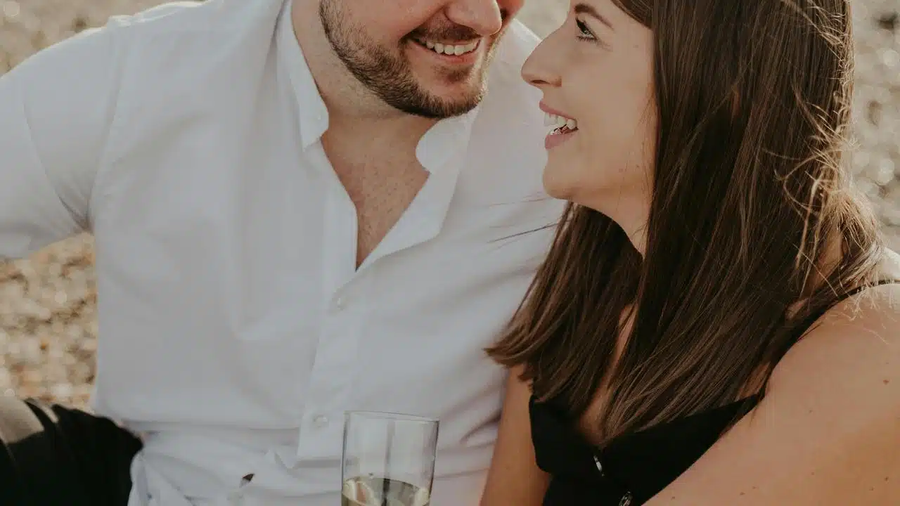 A couple smiling at each other while sitting outdoors with a drink.