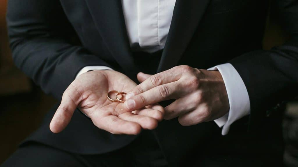 A suited person holding two wedding rings.