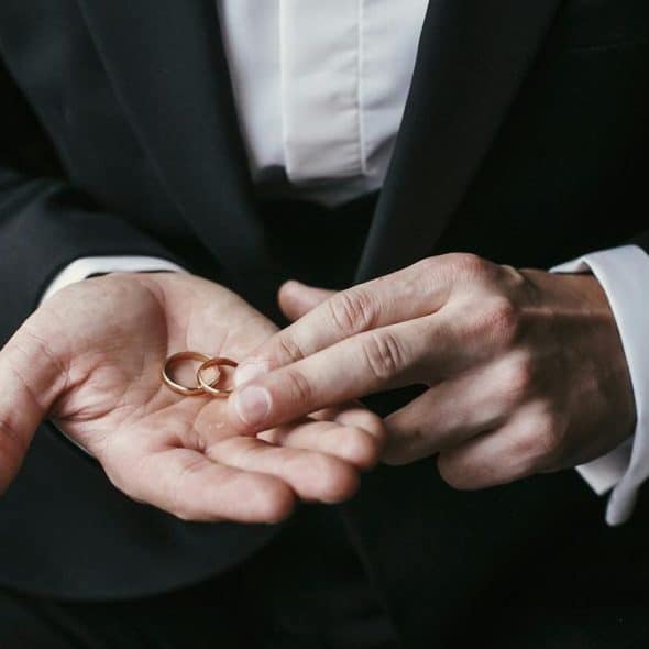 A suited person holding two wedding rings.