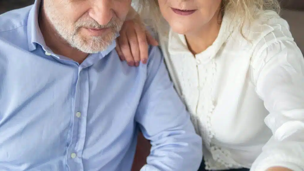 A close-up of a couple sitting together, with one resting a hand on the other’s shoulder.