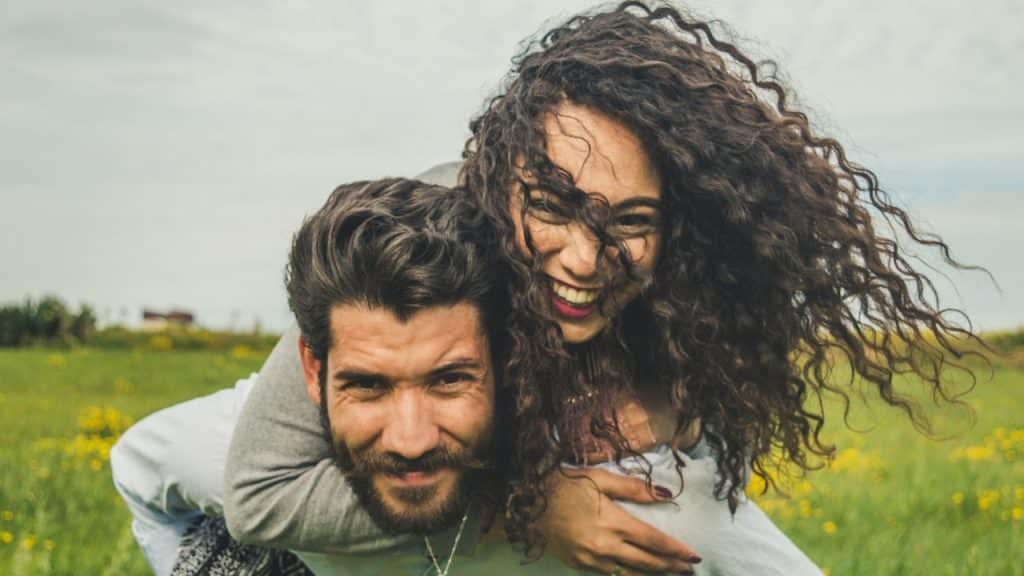 A woman riding on a man's back on a green field.