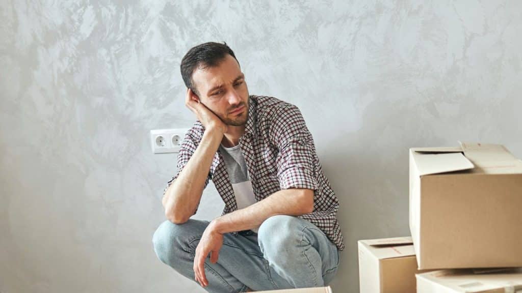 Man looking stressed, crouching by a wall next to moving boxes.