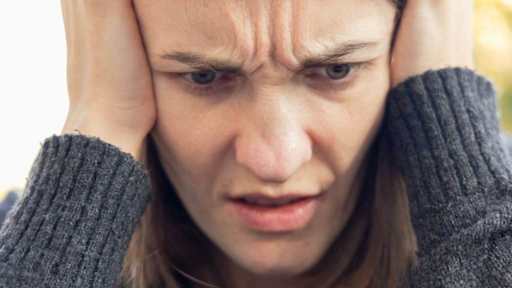 A close-up of a woman in a grey sweater with a pained, angry expression on her face.