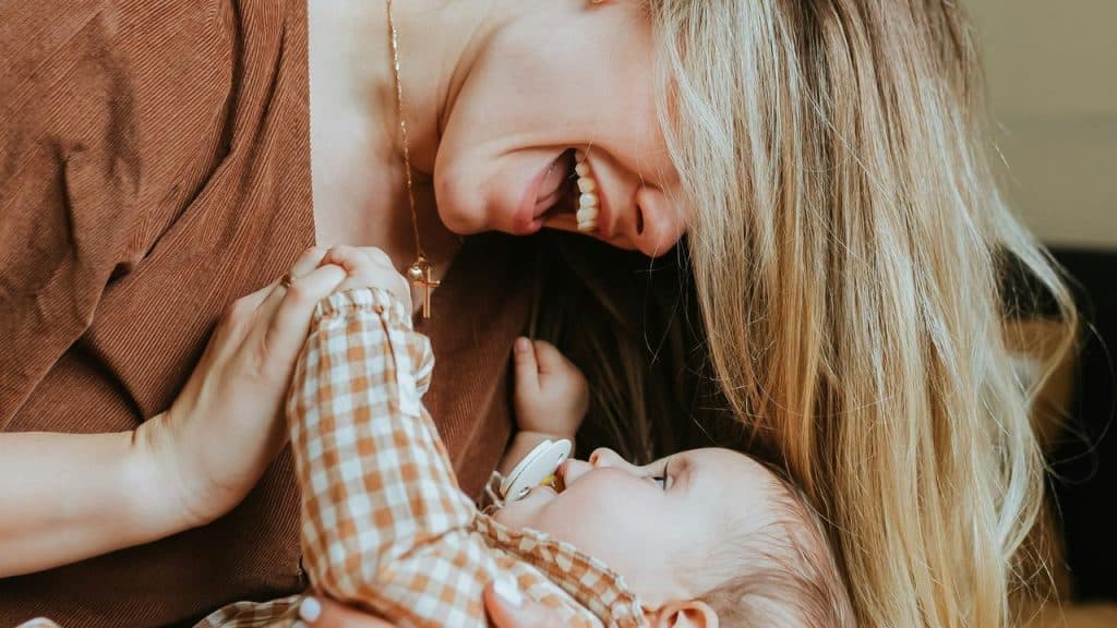 A mother laughing while holding her baby close.