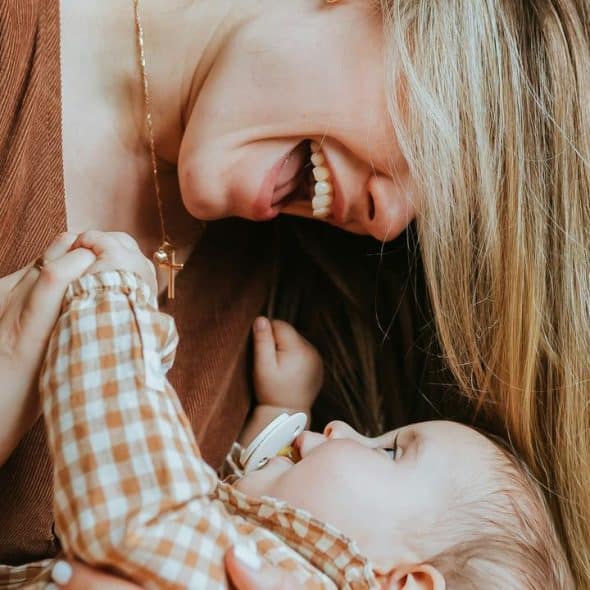 A mother laughing while holding her baby close.