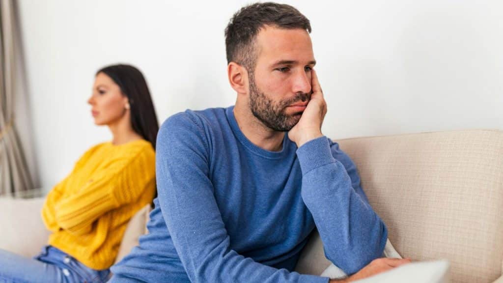A distressed man rests his head on his hand as a woman sits back-to-back with him.