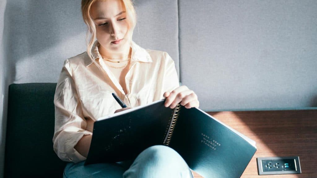 A person writing in a large notebook while seated.