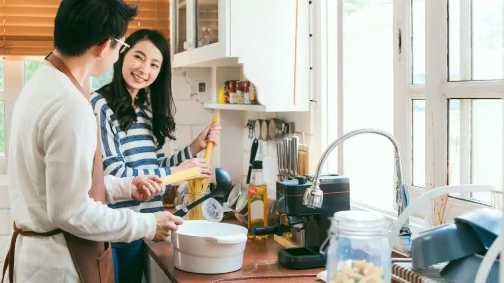 A smiling couple cooks pasta together in a bright kitchen.