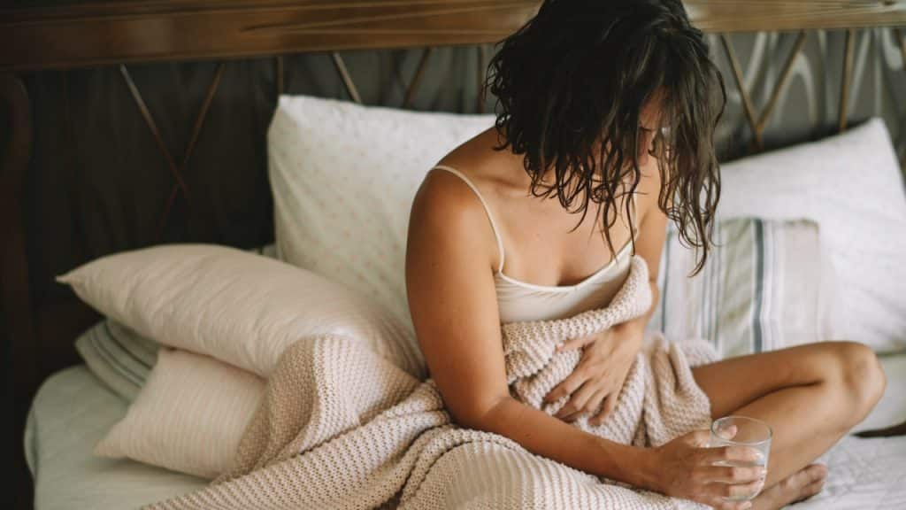 A beautiful woman standing on a bed having stomach pain.