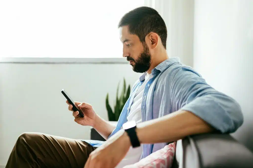 A man sitting on a couch, using his smartphone.