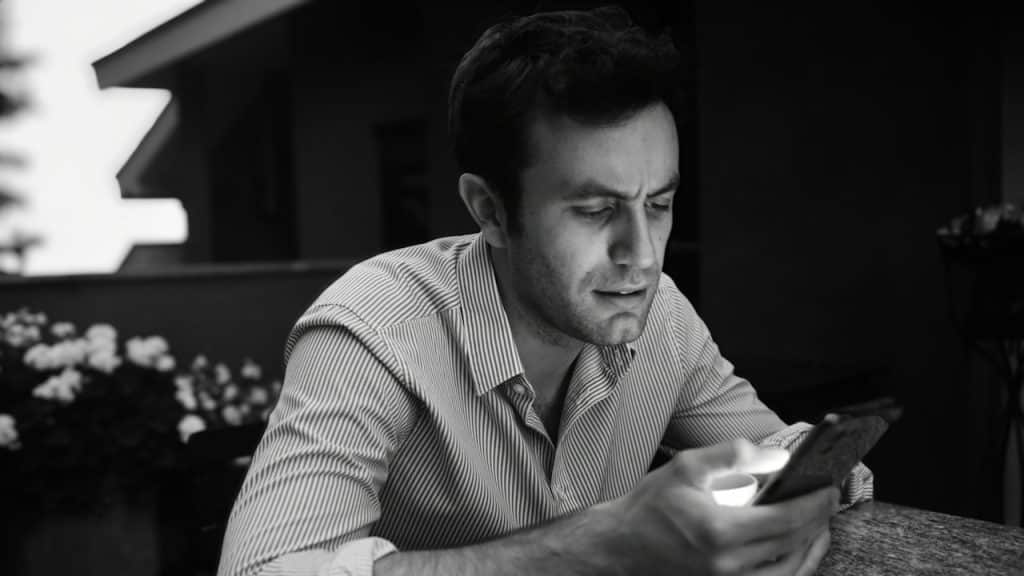 A man looking at his phone while sitting outdoors.