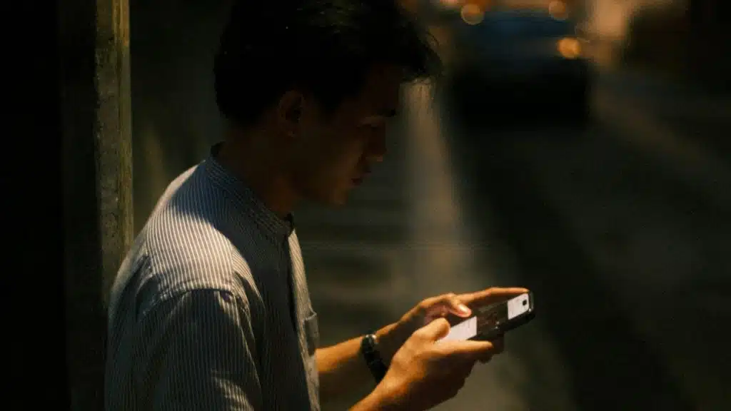 A man standing on a sidewalk looking at his cell phone.