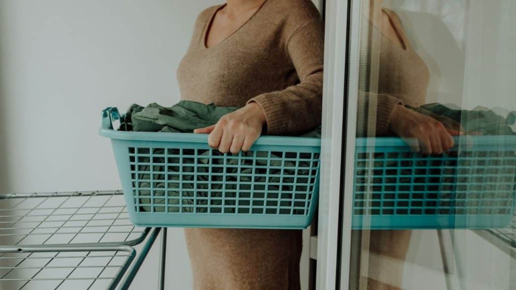 Middle-aged woman in a brown sweater holding a blue laundry basket.