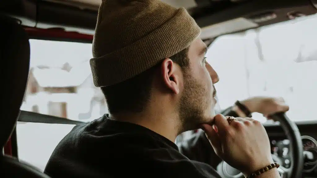 A man wearing a beanie driving while resting his hand on his chin.