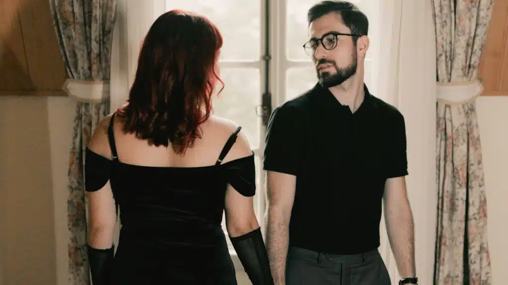 A man and a woman in a black dress are looking at each other while standing next to each other.