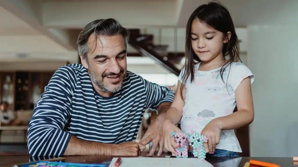 A man and a young girl playing with colorful bead toys at a table.