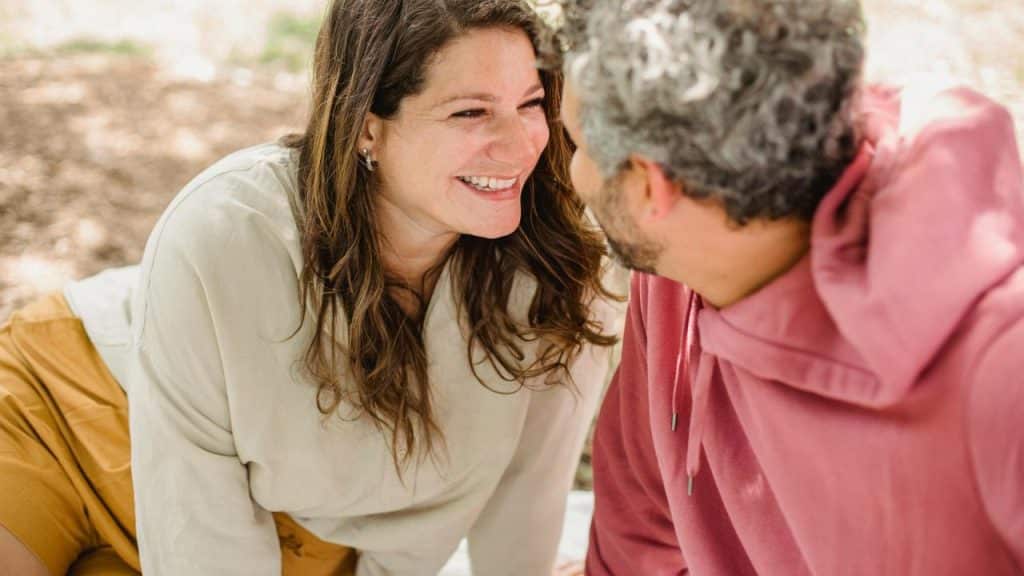 A couple sitting close together and smiling at each other outdoors.