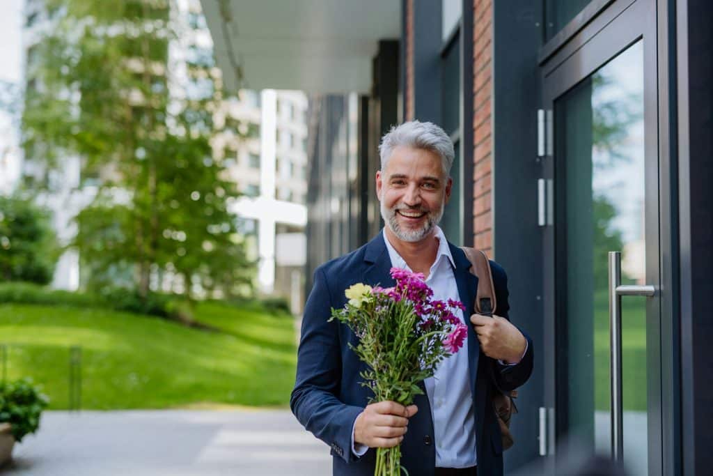 A man walking on the street, holding a bouquet.