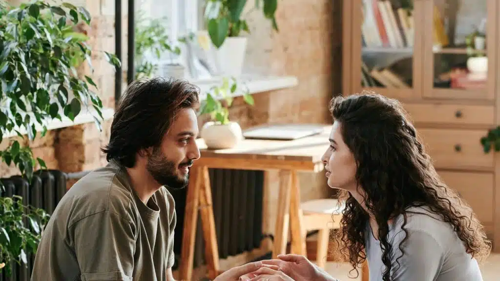 A couple sitting indoors holding hands and talking.