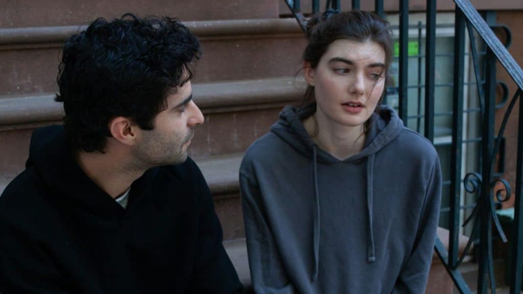A serious-looking man and woman sit side-by-side on outdoor steps.