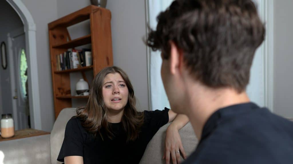 A distressed woman is talking to her husband while sitting on a couch.