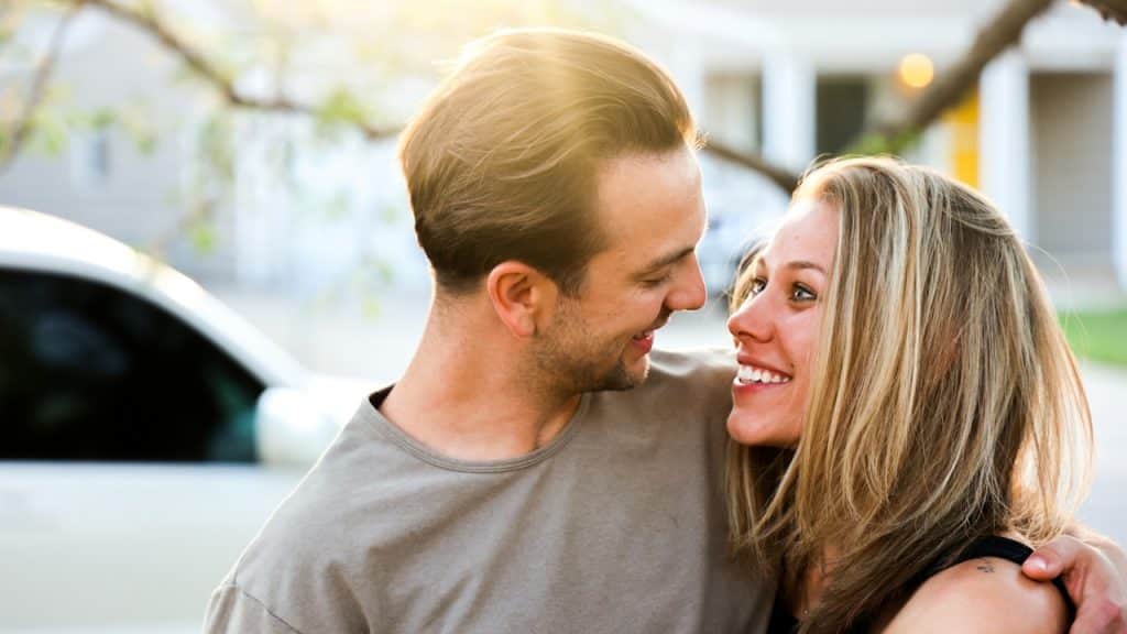 A man and a woman embracing and smiling at each other outdoors in the sunlight.
