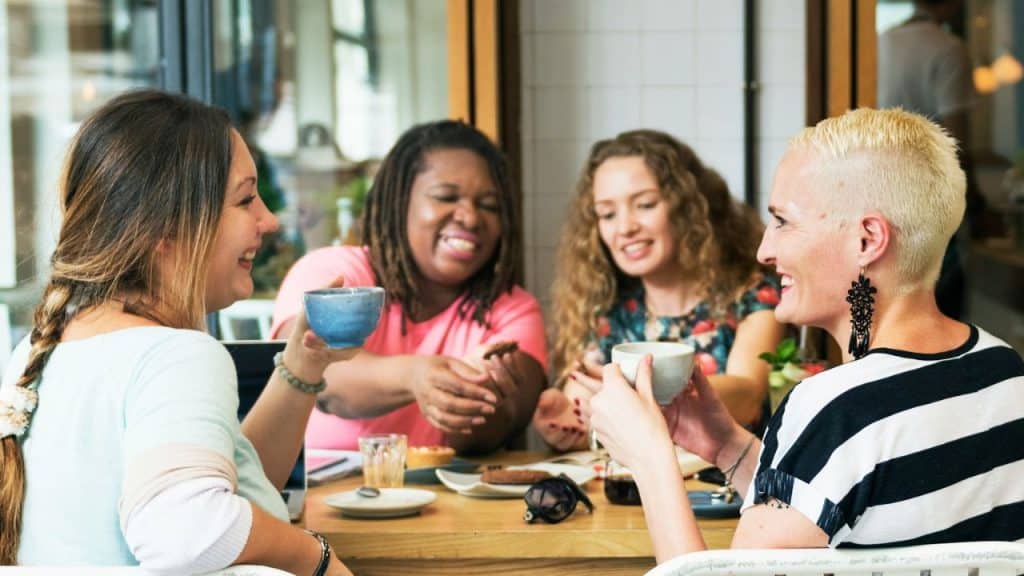 Four women sit around a table with drinks, smiling and engaged in conversation.