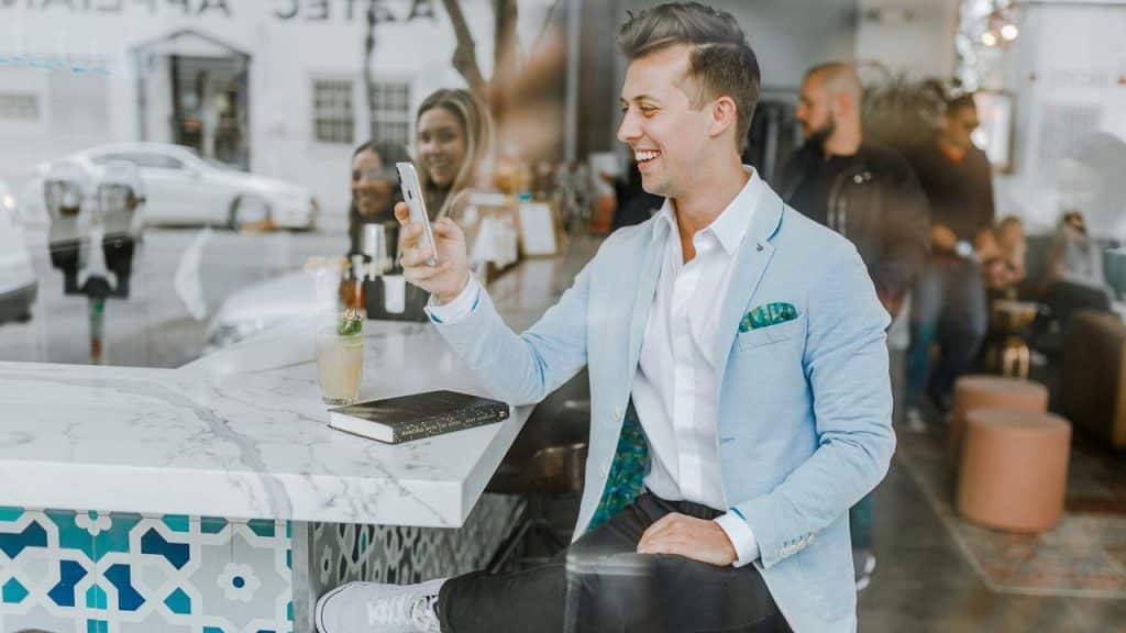 A man sitting at a café counter smiling while looking at his phone.