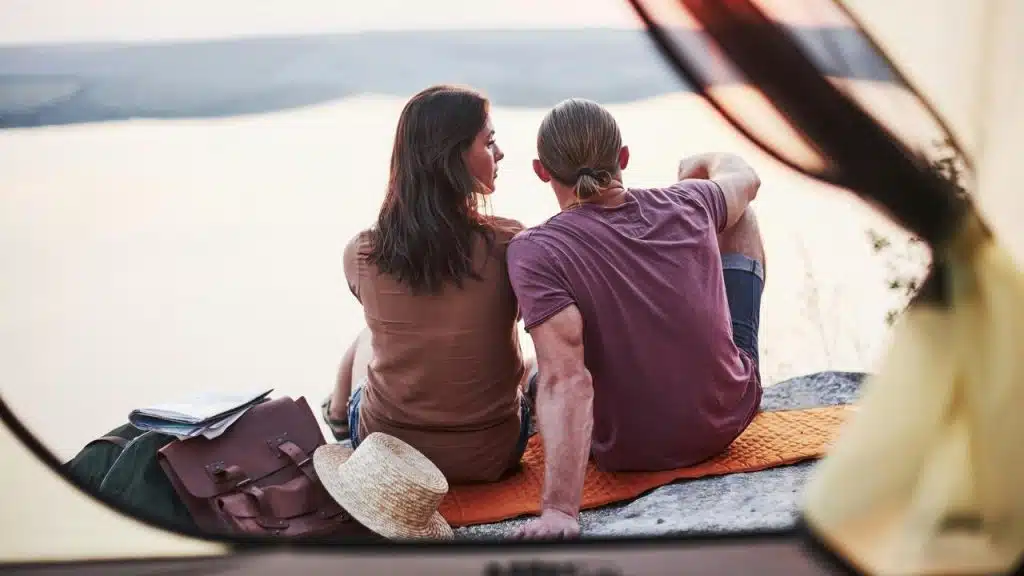 A couple sitting on a blanket by the water, viewed from a tent.