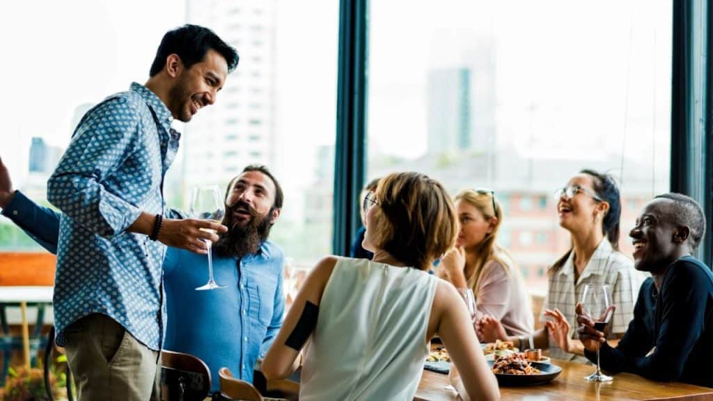 Smiling group of people, some with wine glasses, talking around a table.