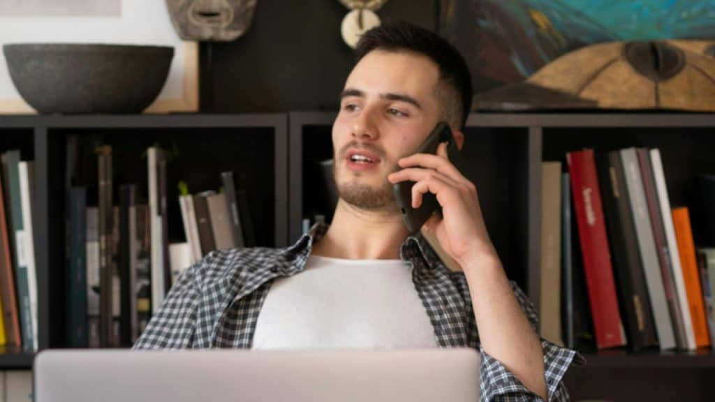 A man talking on a phone while using a laptop.