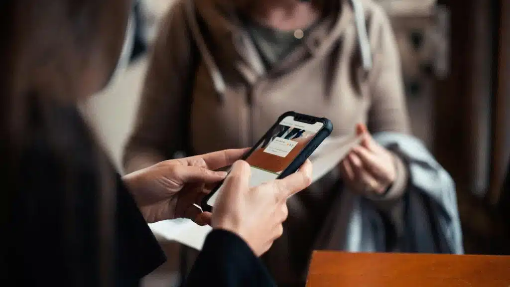 Close-up of a person holding a smartphone displaying a ticket or pass, with another person out of focus in the background.