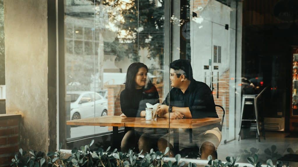 A couple sitting at a table inside a café, looking at each other through the window.