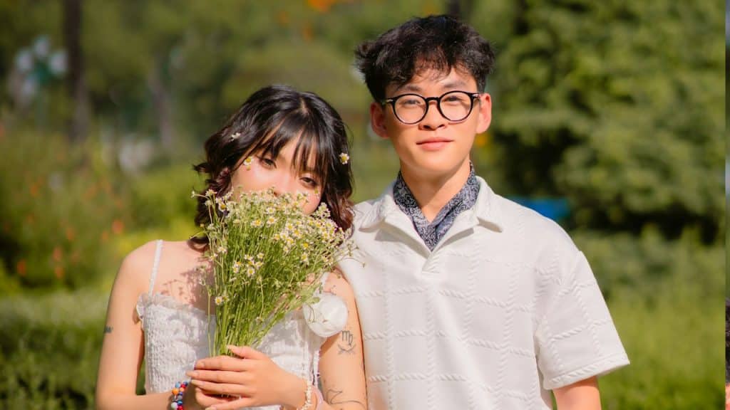 Couple posing in a sunny park with flowers.