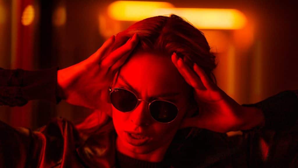 A woman in a black leather jacket wearing black sunglasses.