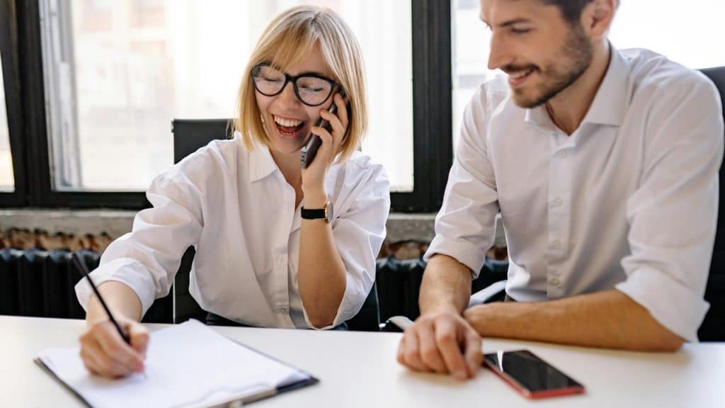 A woman laughing while talking on the phone next to a man.
