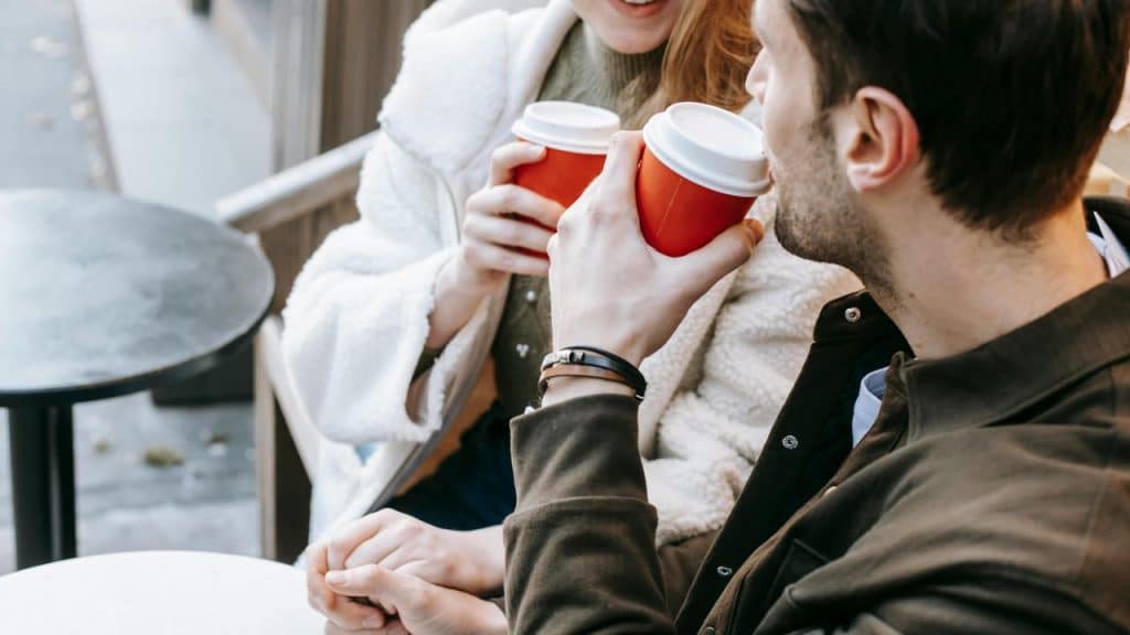 A couple sitting outside holding takeaway coffee cups.