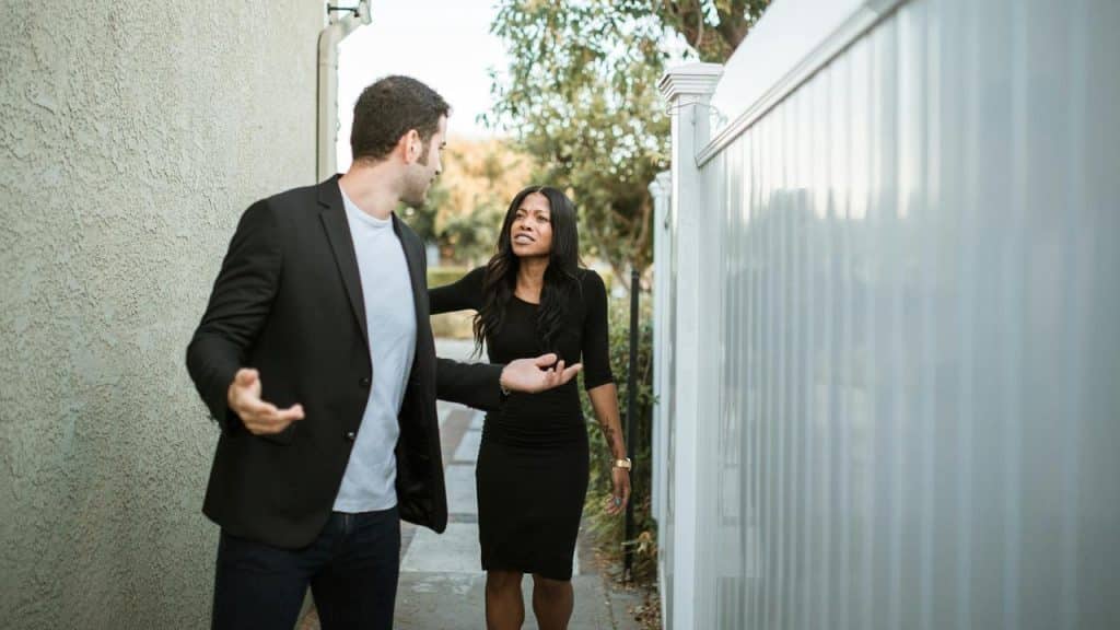 A man and woman arguing while standing in a narrow outdoor walkway.