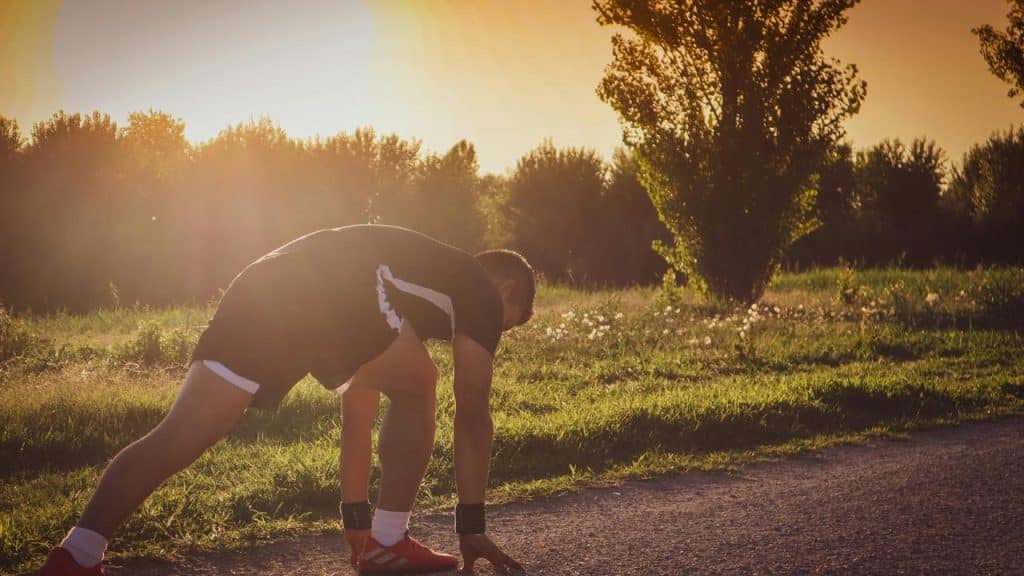 A runner stretching at the start of a path outdoors.