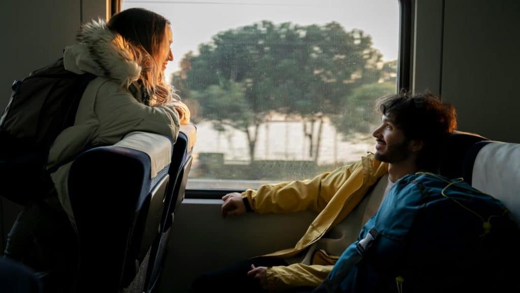 A man and woman sitting on a train talking and smiling at each other.
