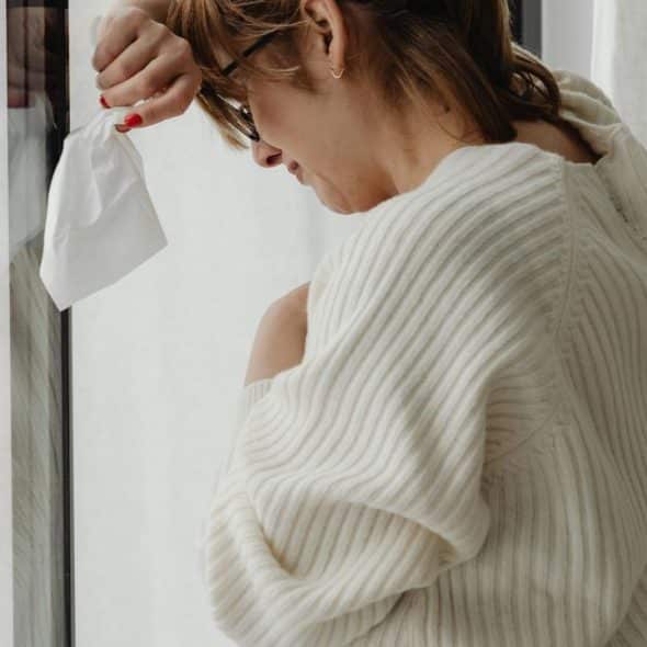A woman holding a tissue and leaning against a window.