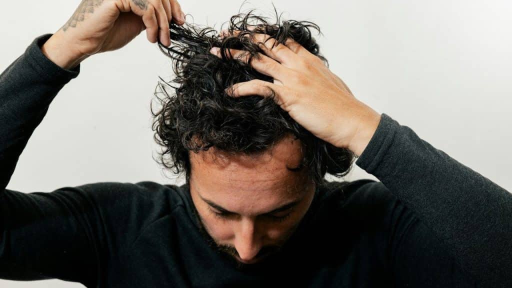 Close-up of a man's hands raking through his dark, curly hair.