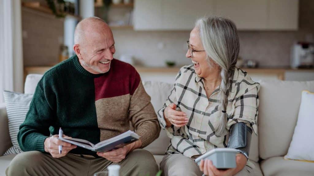 An older couple smiling and laughing while checking blood pressure at home.
