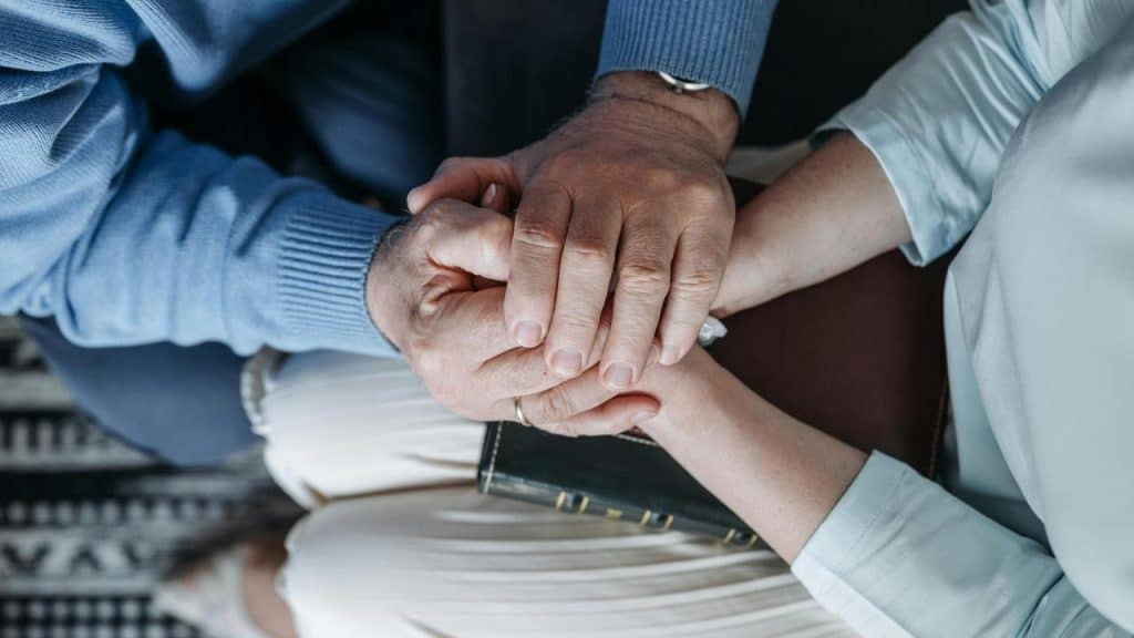 A senior couple holding hands while sitting together.