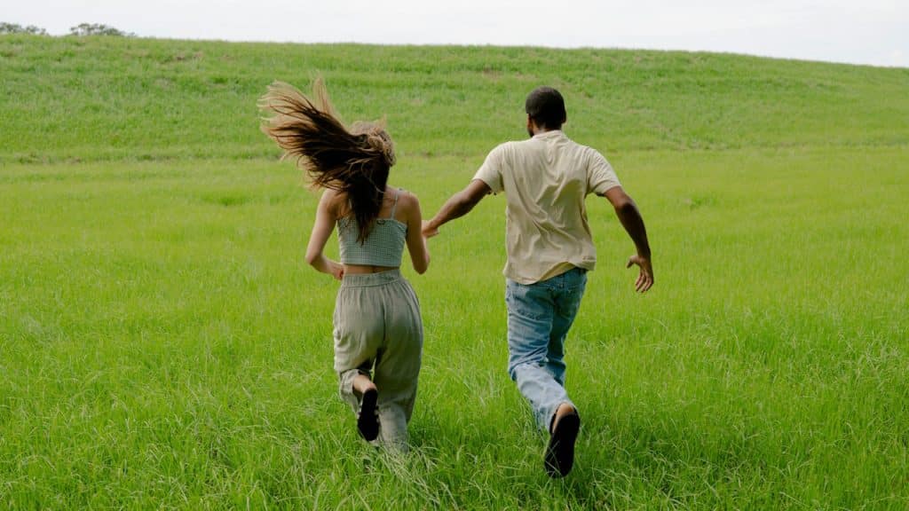 A couple holding hands and running across a grassy landscape together. 