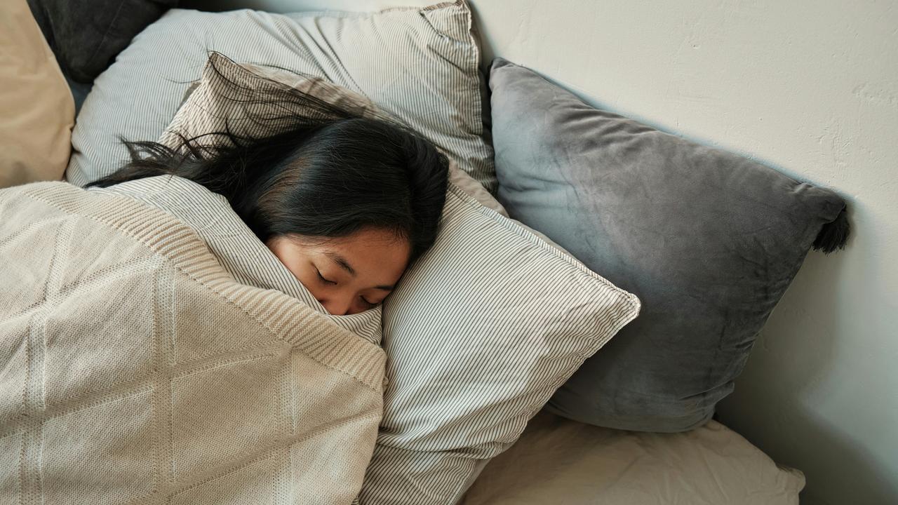 A woman sleeping peacefully under a blanket with pillows around her.