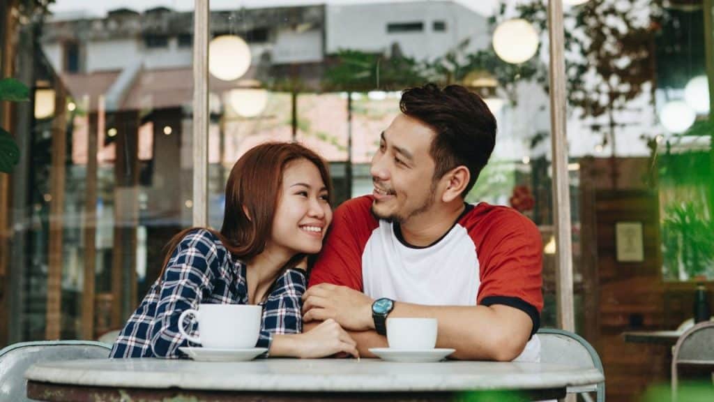 A woman in a plaid shirt smiles while leaning her head against a man’s shoulder.