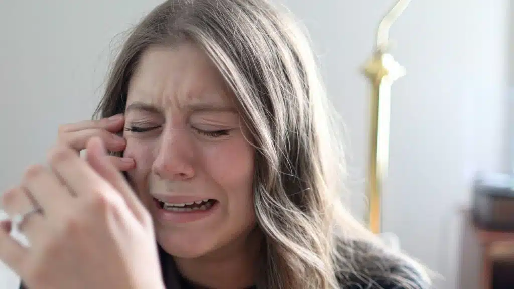 A woman with long hair cries while holding a hand up to her face.